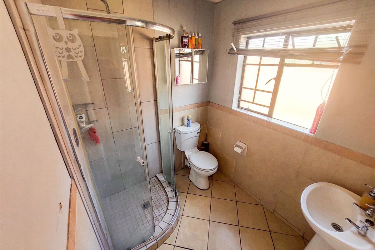A functional bathroom featuring a corner shower enclosure, pedestal basin, and toilet, with tiled flooring and walls requiring cosmetic updates.