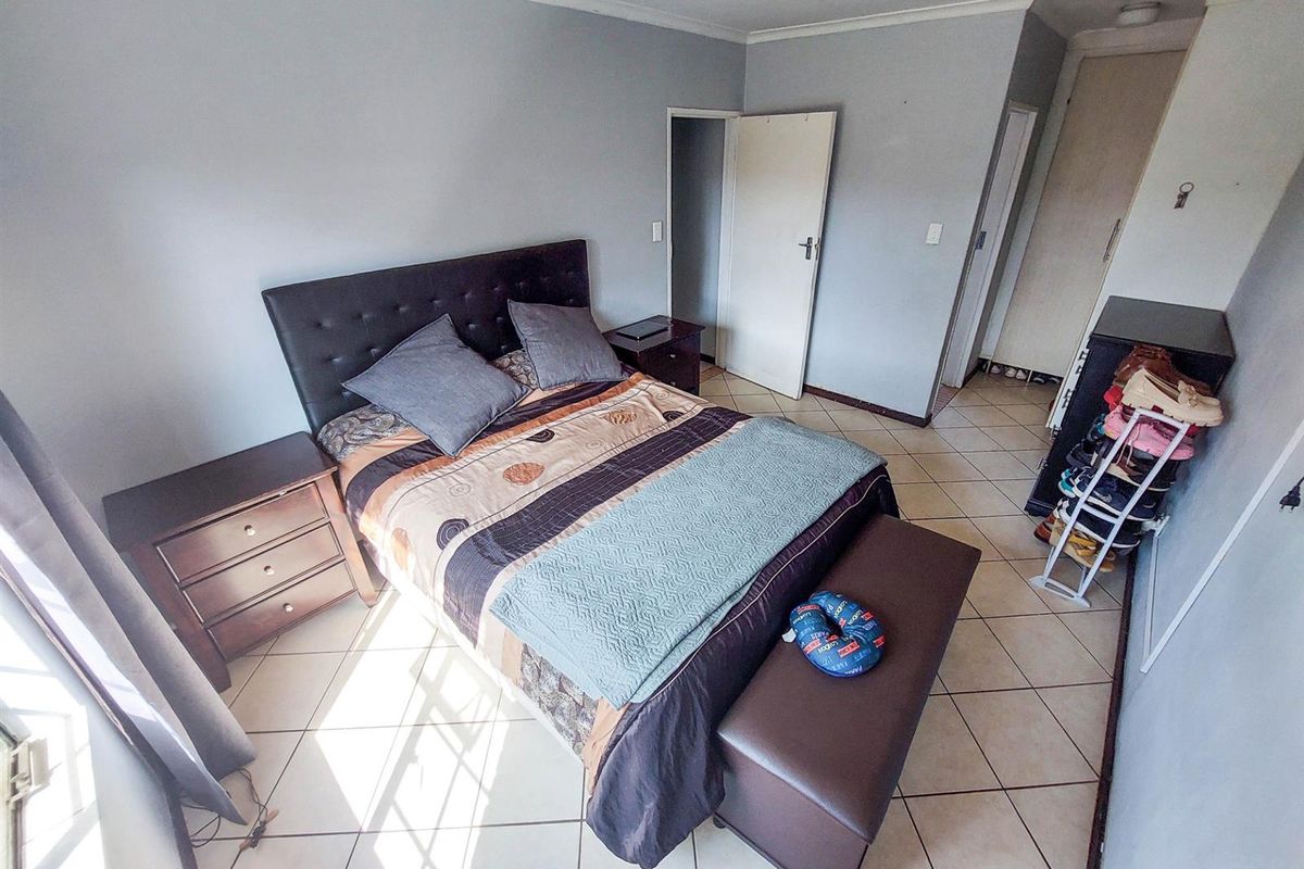 A bedroom featuring tiled flooring, built-in cupboards, and neutral wall tones, providing a functional and well-lit sleeping space.
