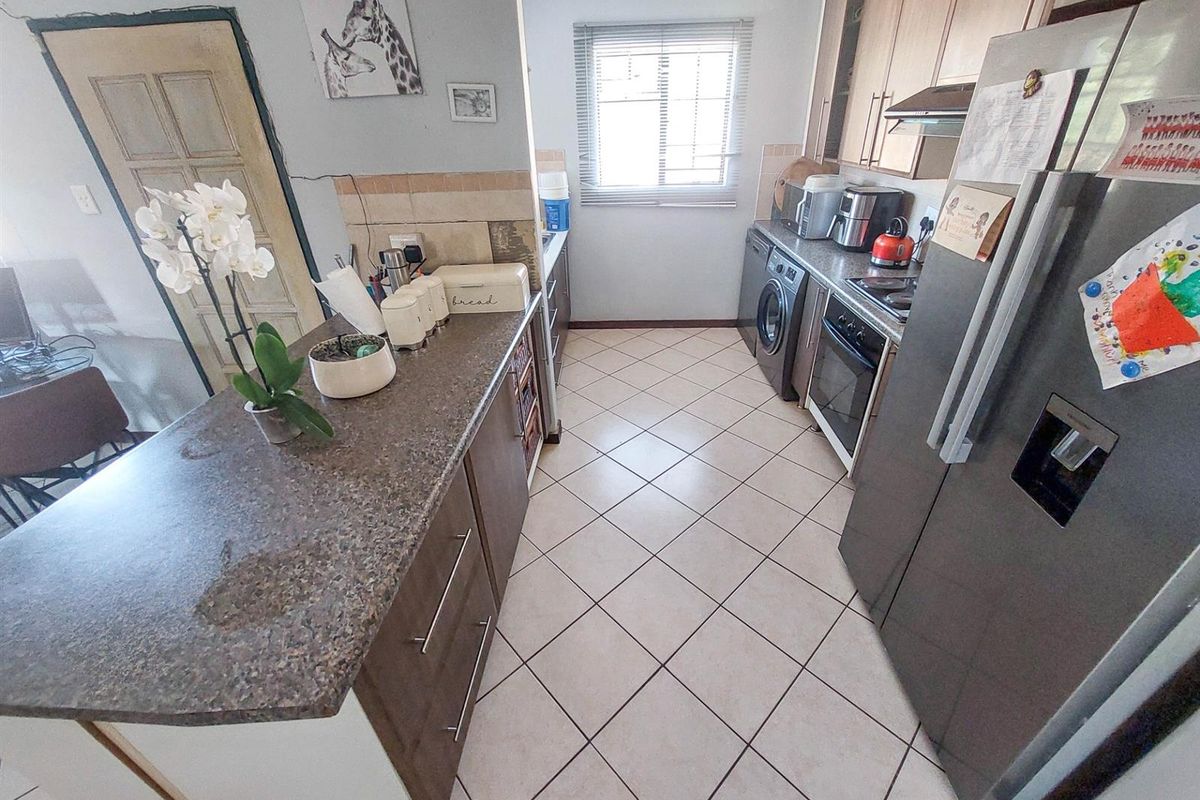 A functional kitchen featuring a breakfast bar, built-in oven, hob, extractor fan, and integrated laundry appliance space with tiled flooring.