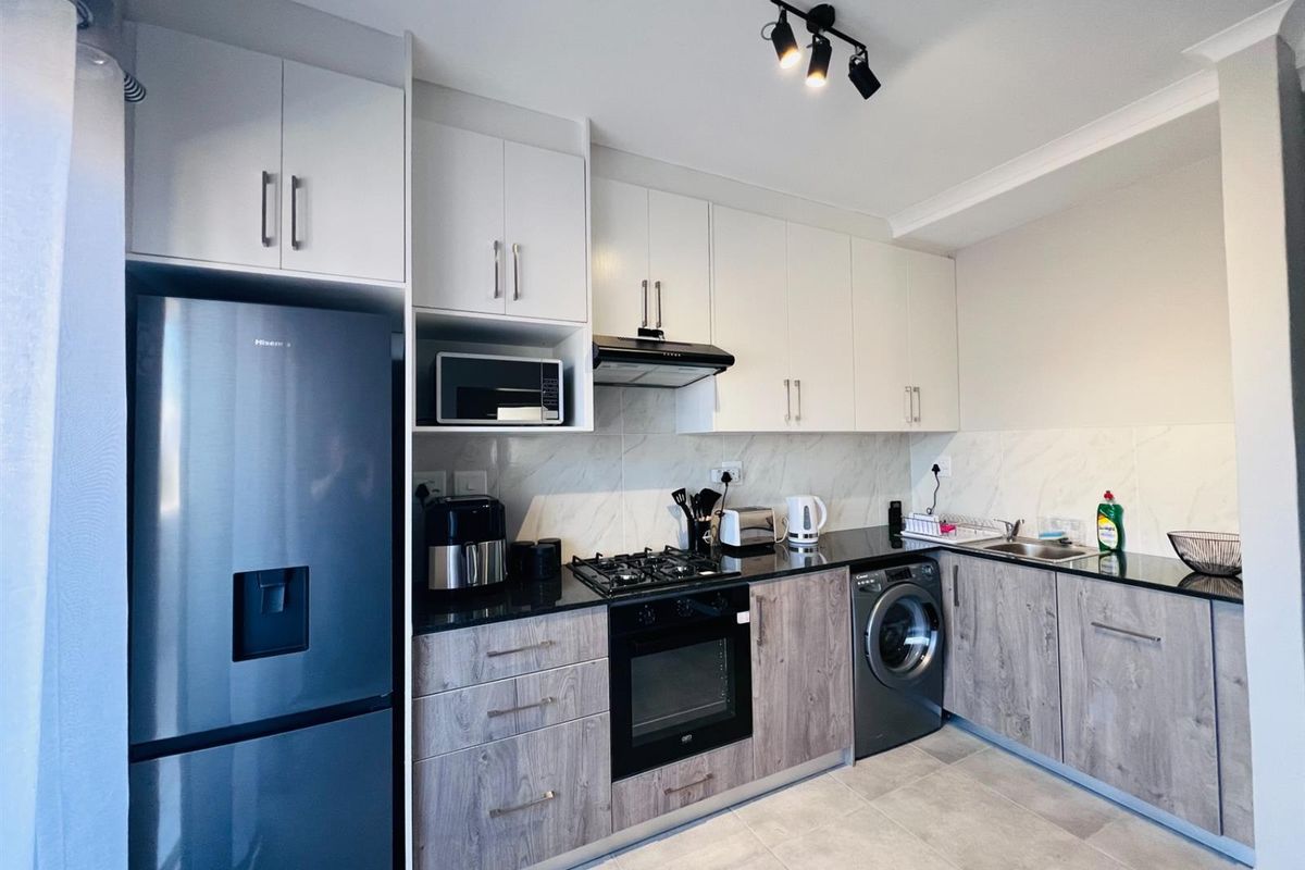 Modern kitchen featuring sleek two-tone cabinetry, black granite countertops, built-in oven, gas hob, extractor fan, and integrated laundry appliance space.