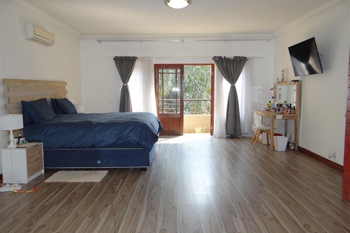 Spacious bedroom featuring light-toned laminate flooring, a split-system air conditioner, and direct access to an outdoor balcony through timber-framed glass doors.