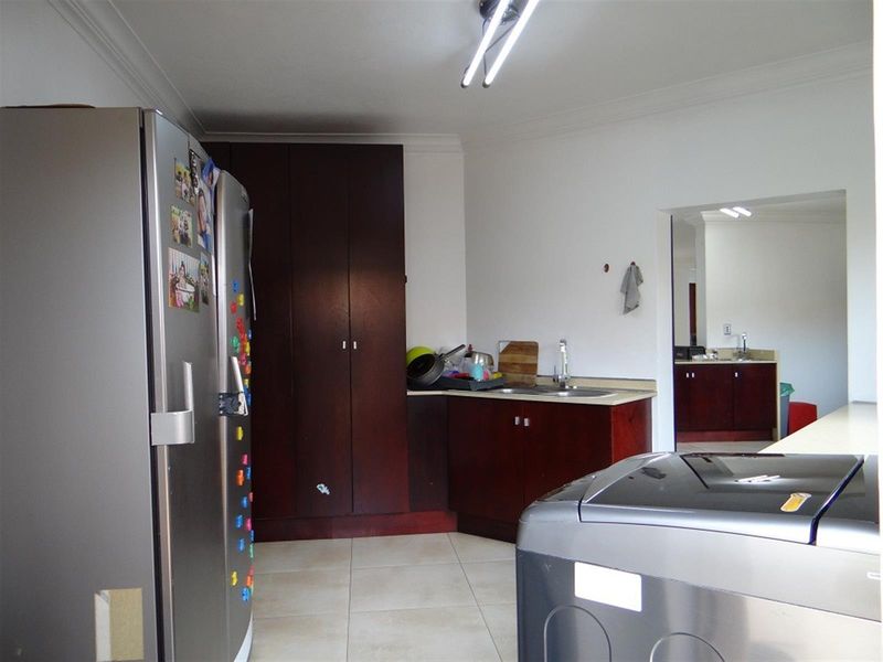A functional laundry room featuring built-in dark wood cabinetry, a sink, and tiled flooring, with direct access to an adjacent utility area.