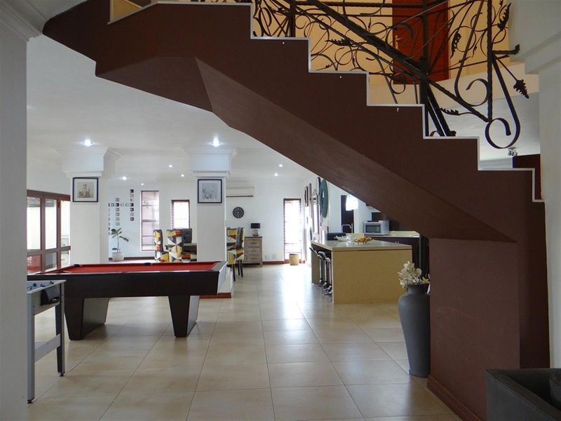 Spacious open-plan living area featuring a prominent staircase with decorative wrought iron railing, tiled floors, and a functional kitchen island.