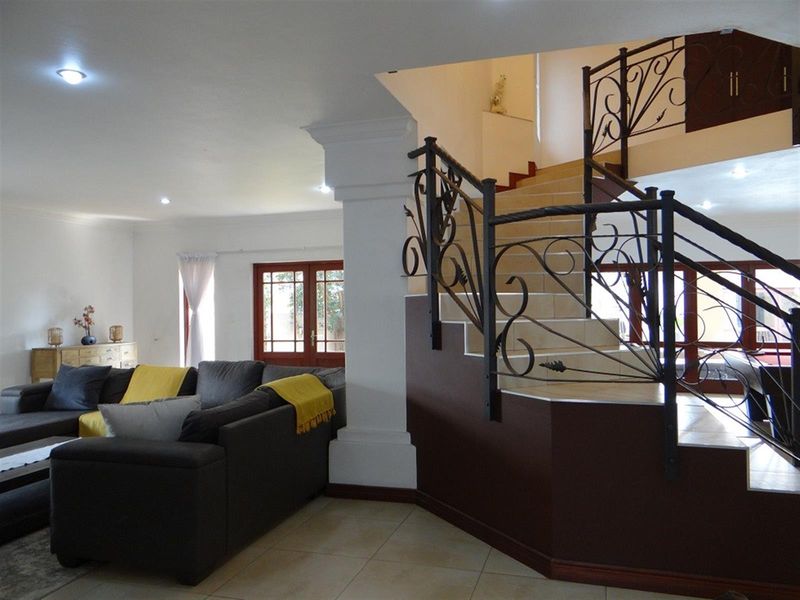 Spacious living area featuring a prominent staircase with decorative wrought iron railings, tiled flooring, and recessed lighting, creating an open and inviting atmosphere.