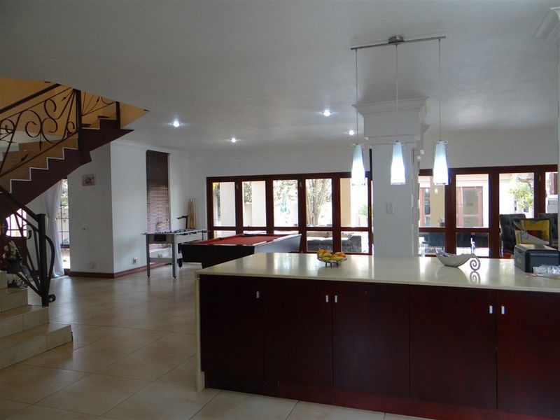 Spacious open-plan living area featuring a kitchen island, tiled flooring, and a decorative wrought iron staircase leading to the upper level.