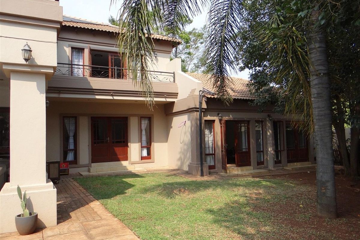 Rear view of a two-story house featuring a paved garden area, wooden framed doors, and an upper-level balcony with wrought iron railings.