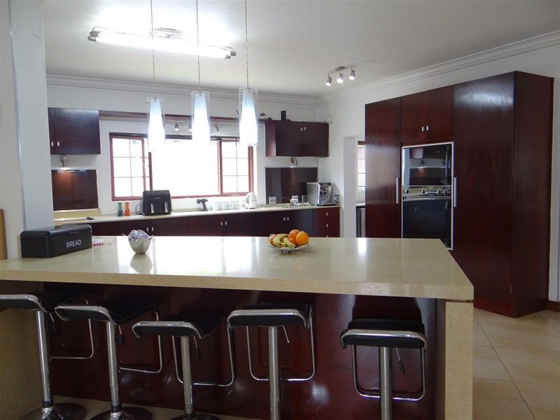 A spacious kitchen featuring dark wood cabinetry, a large central island with stone countertops, built-in appliances, and modern pendant lighting.