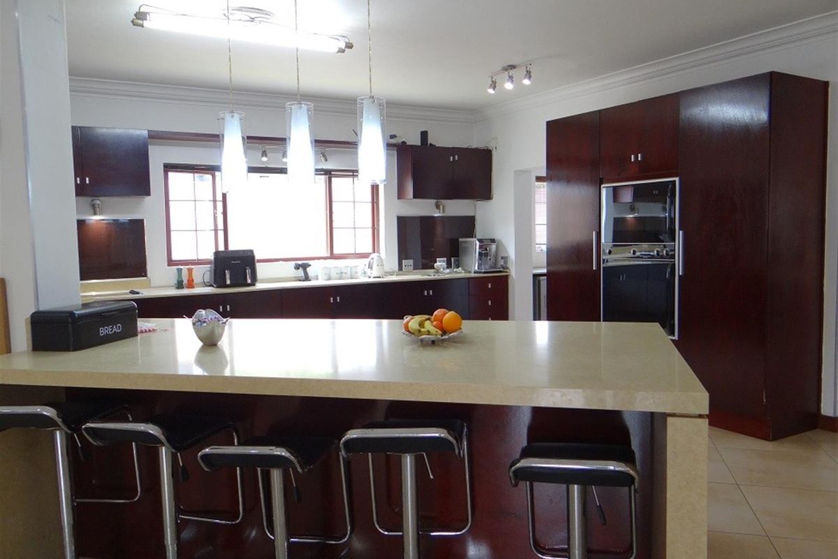 A spacious kitchen featuring dark wood cabinetry, a large central island with stone countertops, built-in appliances, and modern pendant lighting.