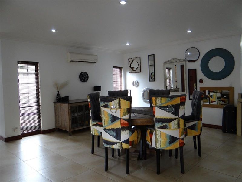 A well-lit dining area featuring neutral tiled flooring, recessed ceiling lighting, and a wall-mounted split-system air conditioning unit.