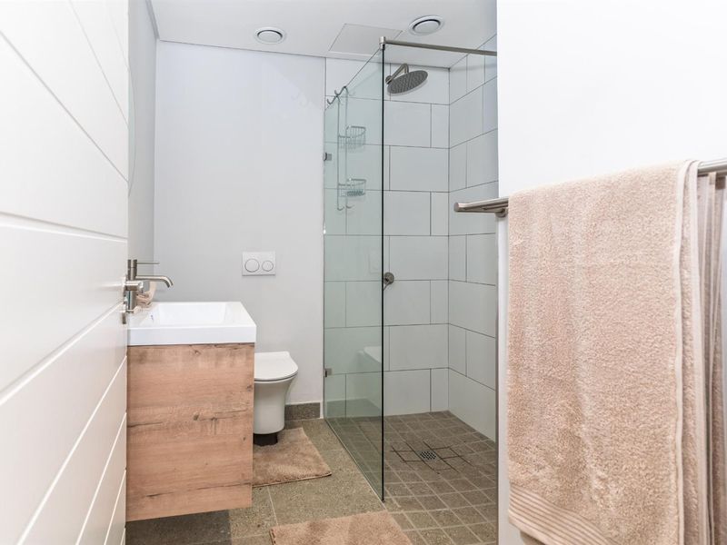 Modern bathroom featuring a walk-in shower with glass screen, wall-hung toilet, and a contemporary vanity unit with basin.