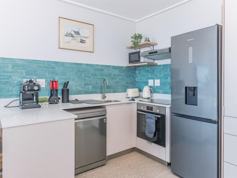 Compact modern kitchen featuring a vibrant teal subway tile backsplash, quartz countertops, stainless steel appliances, and efficient built-in cabinetry.