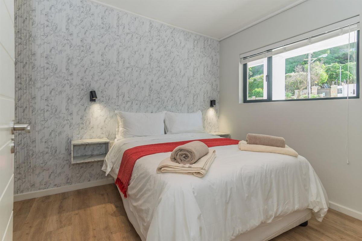 A well-maintained bedroom featuring laminate flooring, marble-effect feature wall, wall-mounted bedside tables, and integrated reading lights.