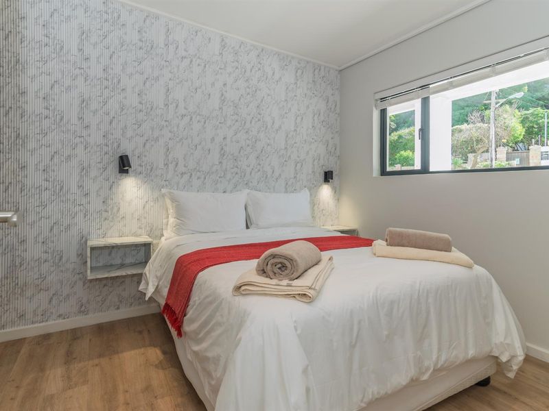 A well-maintained bedroom featuring laminate flooring, marble-effect feature wall, wall-mounted bedside tables, and integrated reading lights.