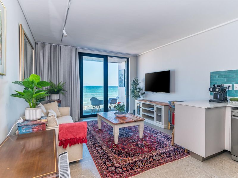 Open-plan living area featuring a kitchenette with a blue tiled backsplash and large sliding doors opening to a balcony with ocean views.
