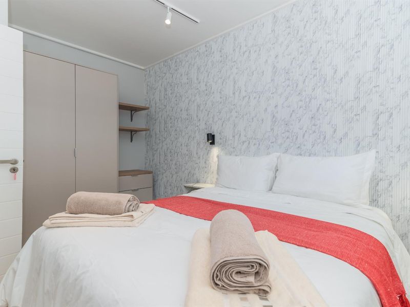 A well-maintained bedroom featuring built-in wardrobe storage, modern track lighting, wall sconce fixtures, and decorative textured wallpaper.