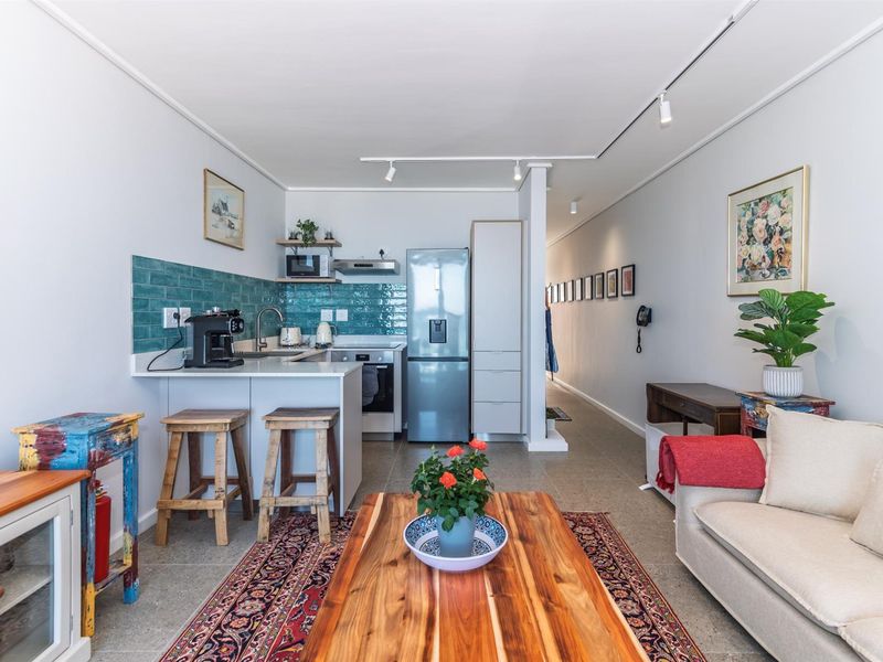 Open-plan living area featuring a modern kitchen with teal subway tile backsplash, built-in cabinetry, and integrated appliances, flowing into a bright, tiled living space.
