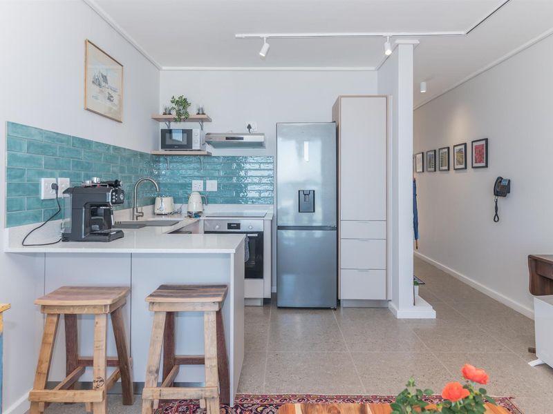 Modern kitchen featuring sleek white cabinetry, quartz countertops, a vibrant teal subway tile backsplash, and integrated stainless steel appliances.
