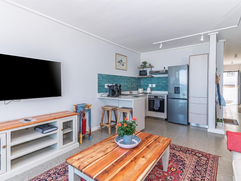 An open-plan living area featuring a compact kitchen with a tiled backsplash, built-in oven, extractor fan, and modern cabinetry.