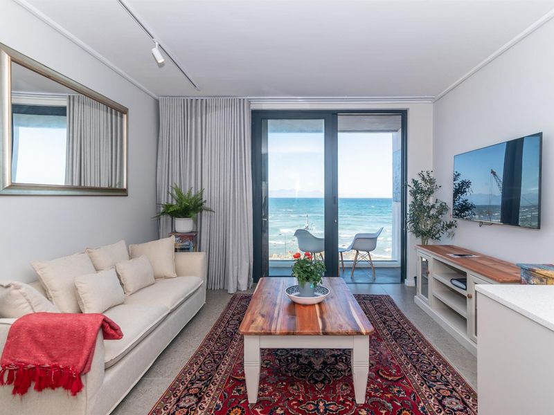 Bright living room featuring tiled flooring, modern track lighting, and large sliding glass doors opening to a balcony with ocean views.