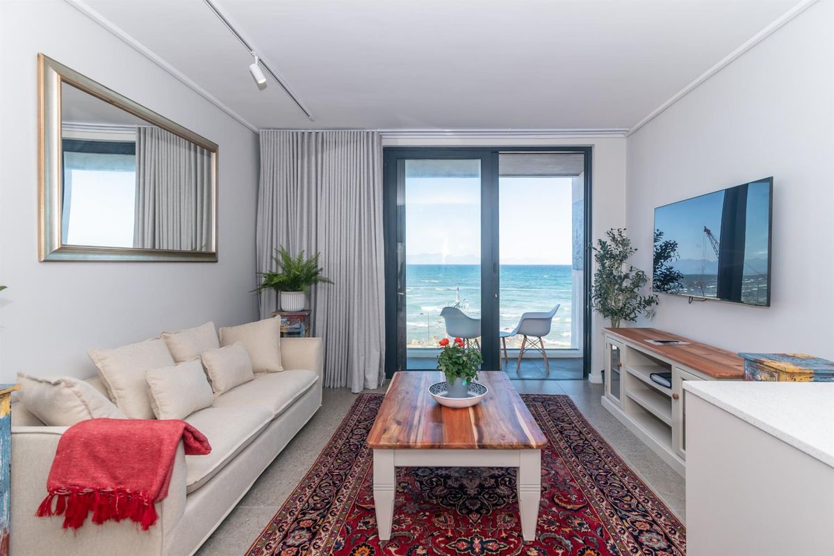 Bright living room featuring tiled flooring, modern track lighting, and large sliding glass doors opening to a balcony with ocean views.