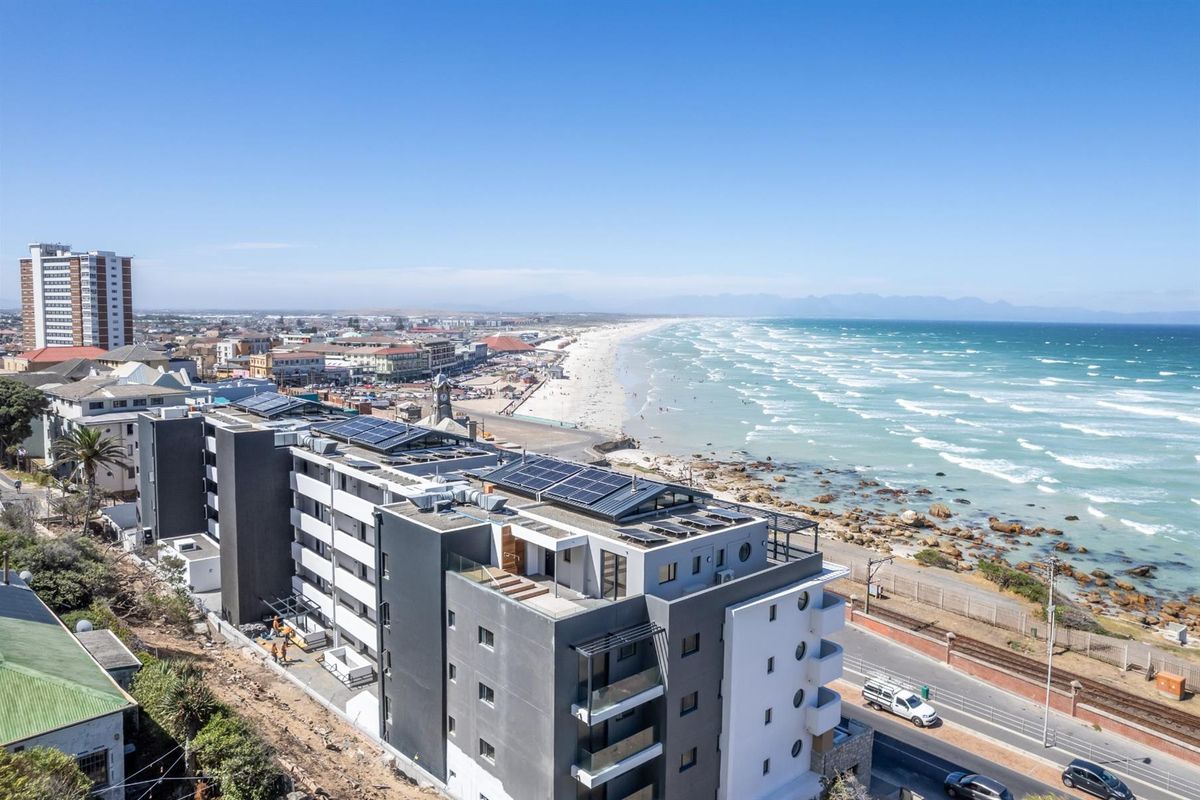 Aerial view of a modern apartment complex situated directly along the coastline, featuring rooftop solar panels and private balconies.