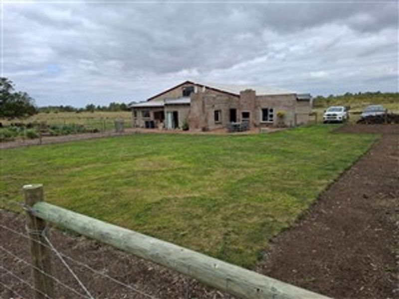 A view of the rear exterior of the farm property, featuring a spacious lawn, brick facade, and outdoor entertainment area.