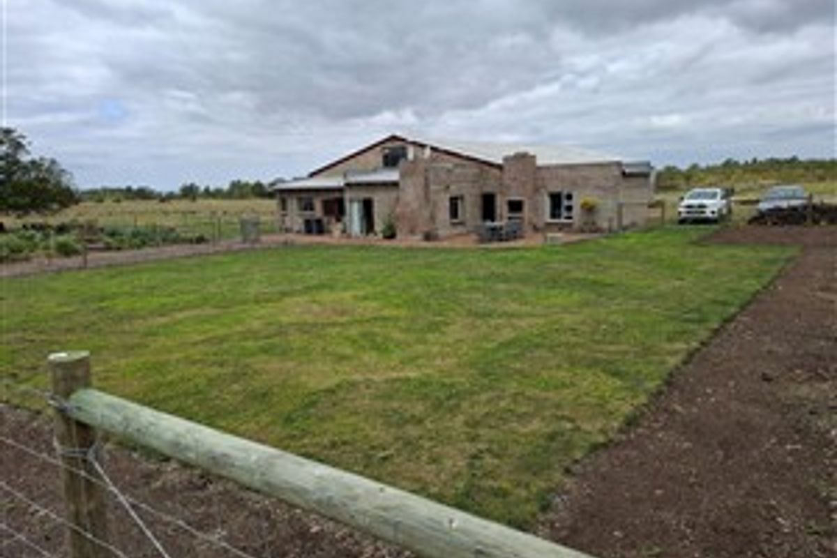 A view of the rear exterior of the farm property, featuring a spacious lawn, brick facade, and outdoor entertainment area.