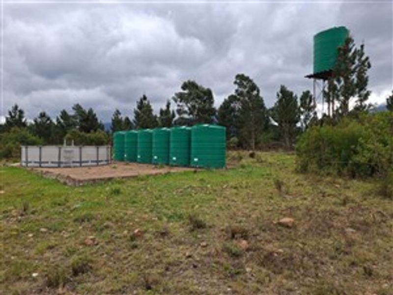 Outdoor farm area featuring multiple large green water storage tanks and a circular reservoir tank on a concrete base.