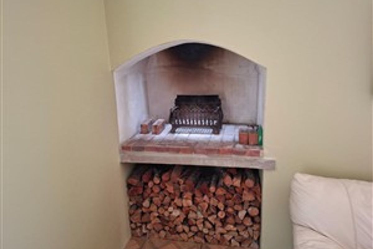 A traditional built-in indoor fireplace featuring a brick hearth and integrated log storage compartment below.