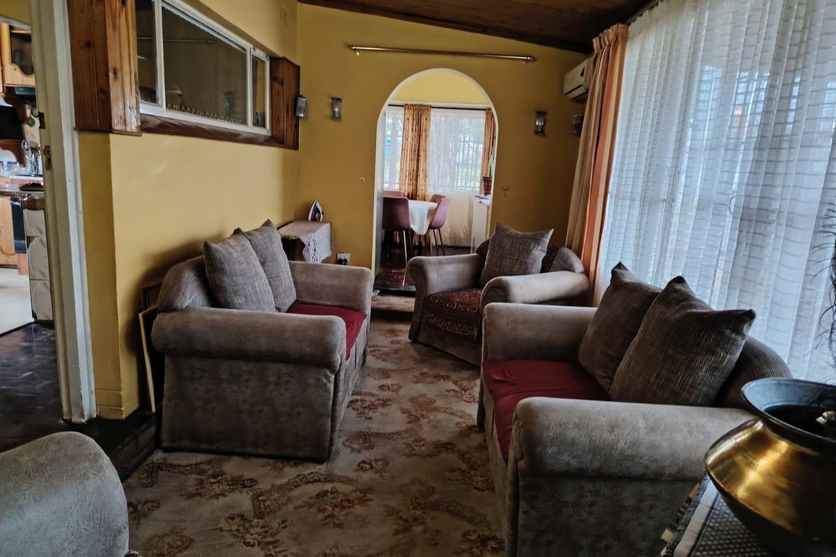 A living room featuring an arched doorway leading to a dining area, wood-paneled ceiling, and large windows with curtains.