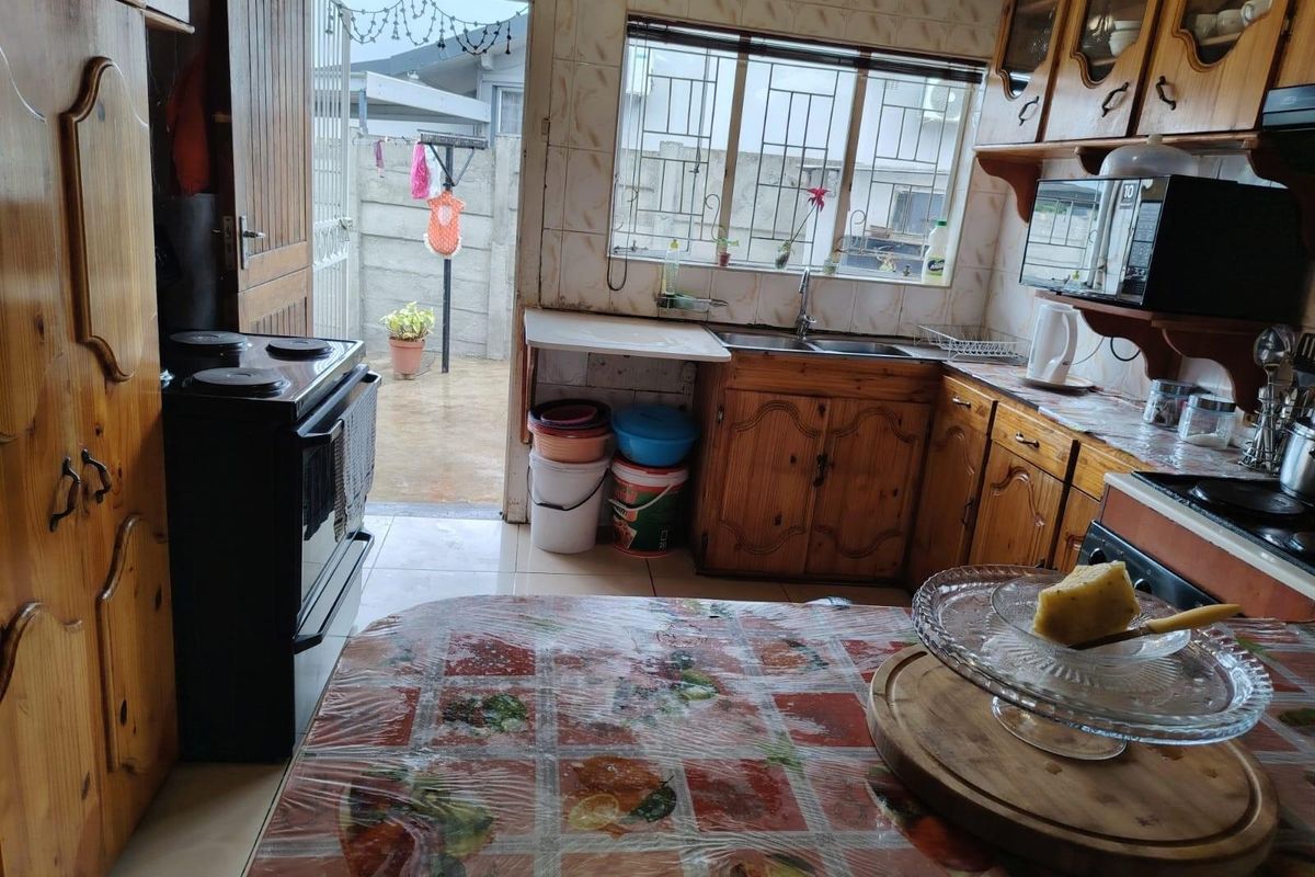 A dated kitchen featuring wooden cabinetry, tiled walls, and a direct access point to the rear exterior area.
