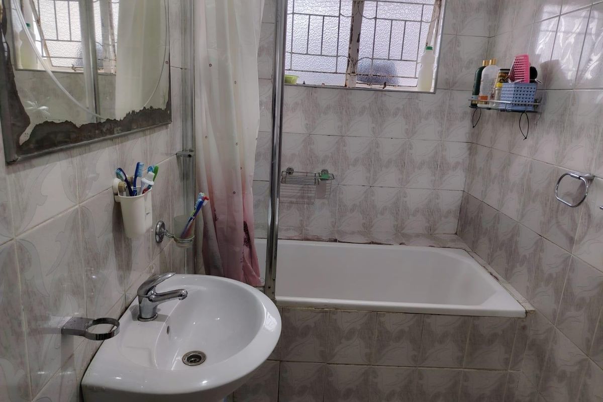 A compact bathroom featuring a pedestal basin, a built-in bathtub with a shower curtain, and full-height wall tiling.