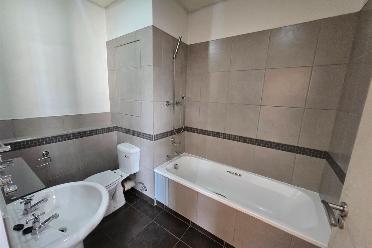 A functional bathroom featuring a bathtub with shower attachment, pedestal basin, and toilet, finished with neutral wall and floor tiling.