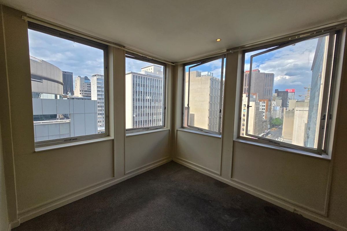 An empty corner room featuring large windows with expansive city views and neutral carpeting.