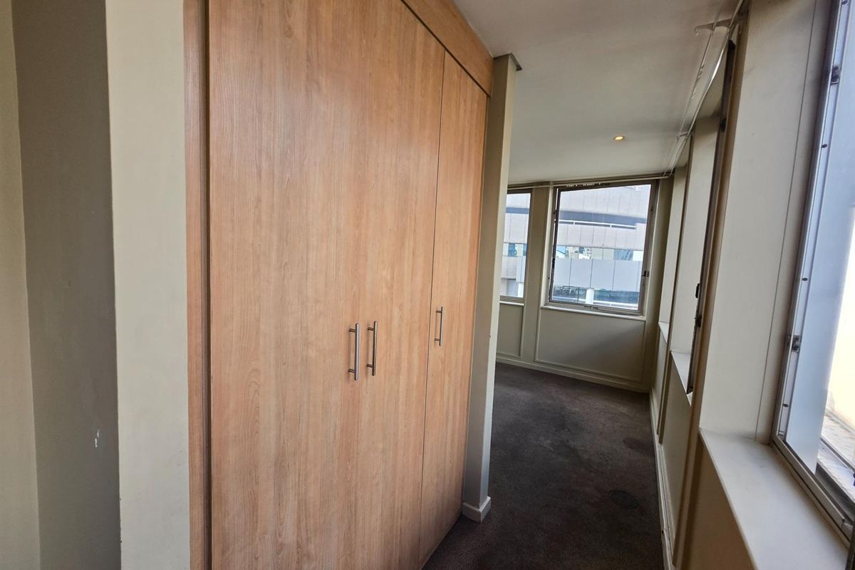 A bedroom featuring built-in wooden cabinetry and large windows providing natural light and urban views.