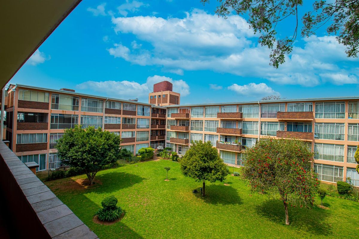 View of the apartment complex exterior, featuring a well-maintained communal garden area and multiple residential balconies.