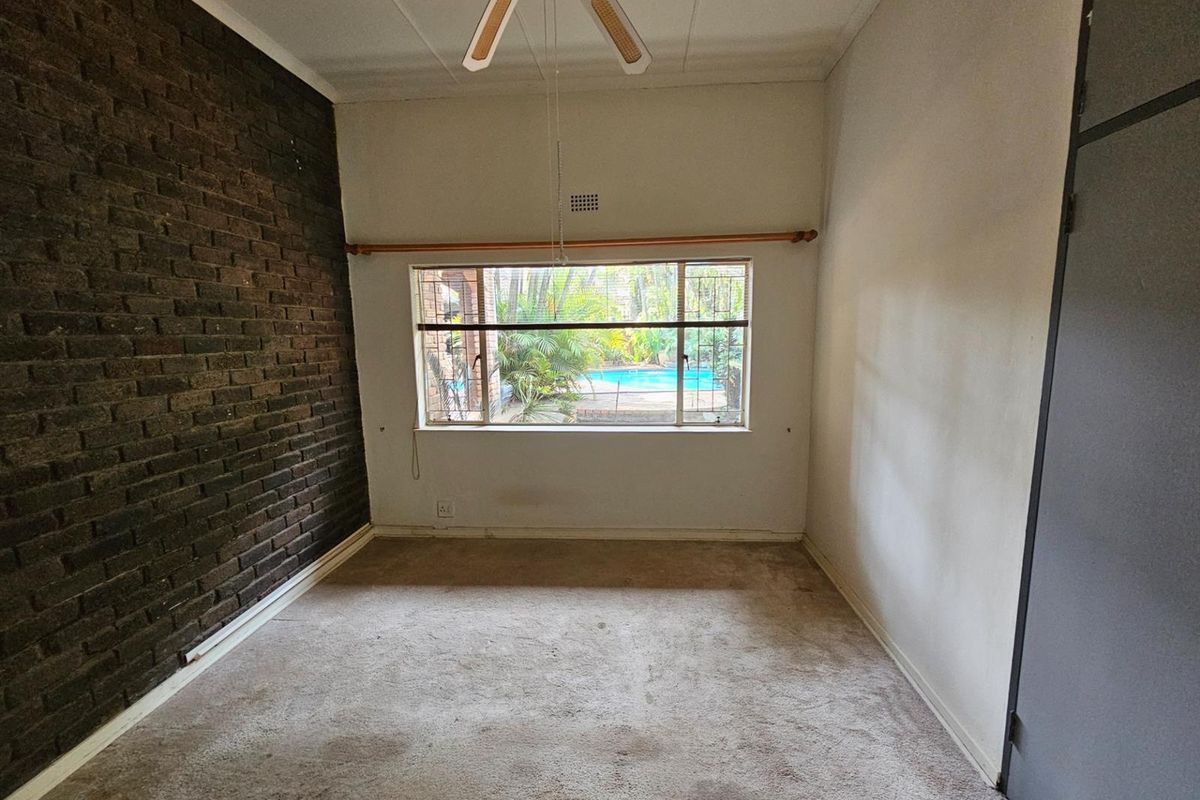 A bedroom featuring a dark brick accent wall, carpeted flooring, and a window view overlooking the pool area.