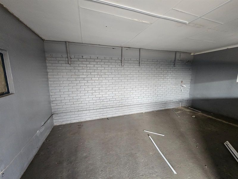 An empty industrial utility space featuring painted brick walls, concrete flooring, and a suspended ceiling, suitable for storage or workshop use.