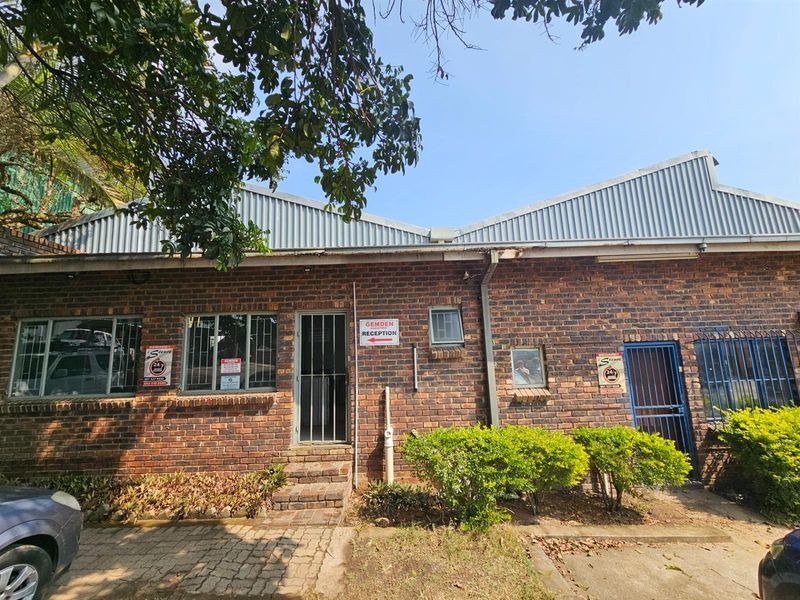 Industrial property exterior featuring face-brick facade, corrugated metal roof, security gates, and metal-framed windows with security bars.