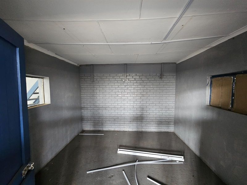 An empty industrial utility space featuring painted brick walls, a suspended ceiling, and concrete flooring, suitable for storage or workshop use.