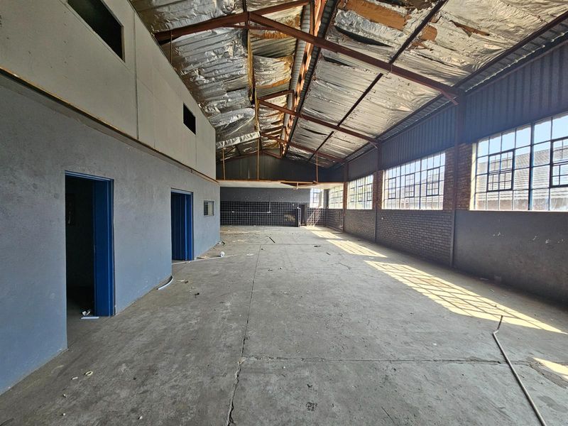 Spacious industrial warehouse area featuring high ceilings, exposed roof structure, large windows for natural light, and concrete flooring.