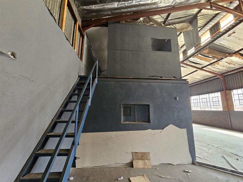 Industrial warehouse interior featuring a two-level mezzanine structure with metal staircase and exposed roof trusses in need of significant repair.