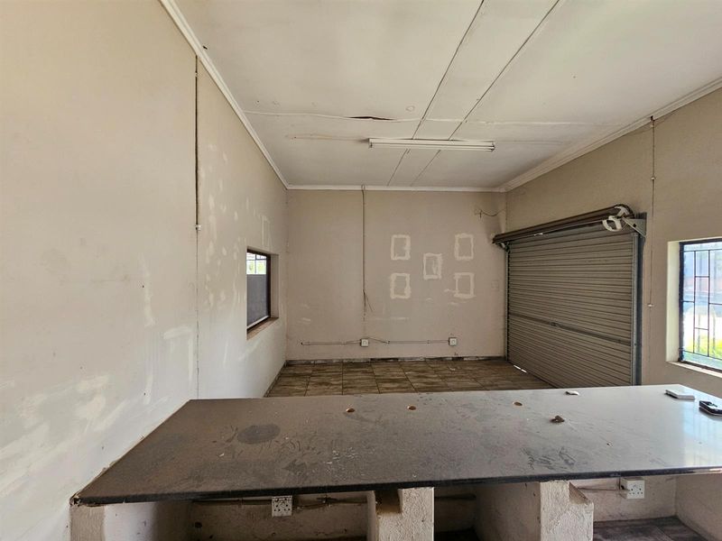 Industrial utility space featuring a roller shutter door, tiled flooring, and a built-in service counter, suitable for workshop or storage use.