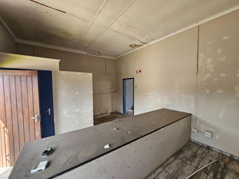 Industrial interior space featuring a built-in service counter, tiled flooring, and multiple access points, requiring significant renovation and cosmetic repairs.
