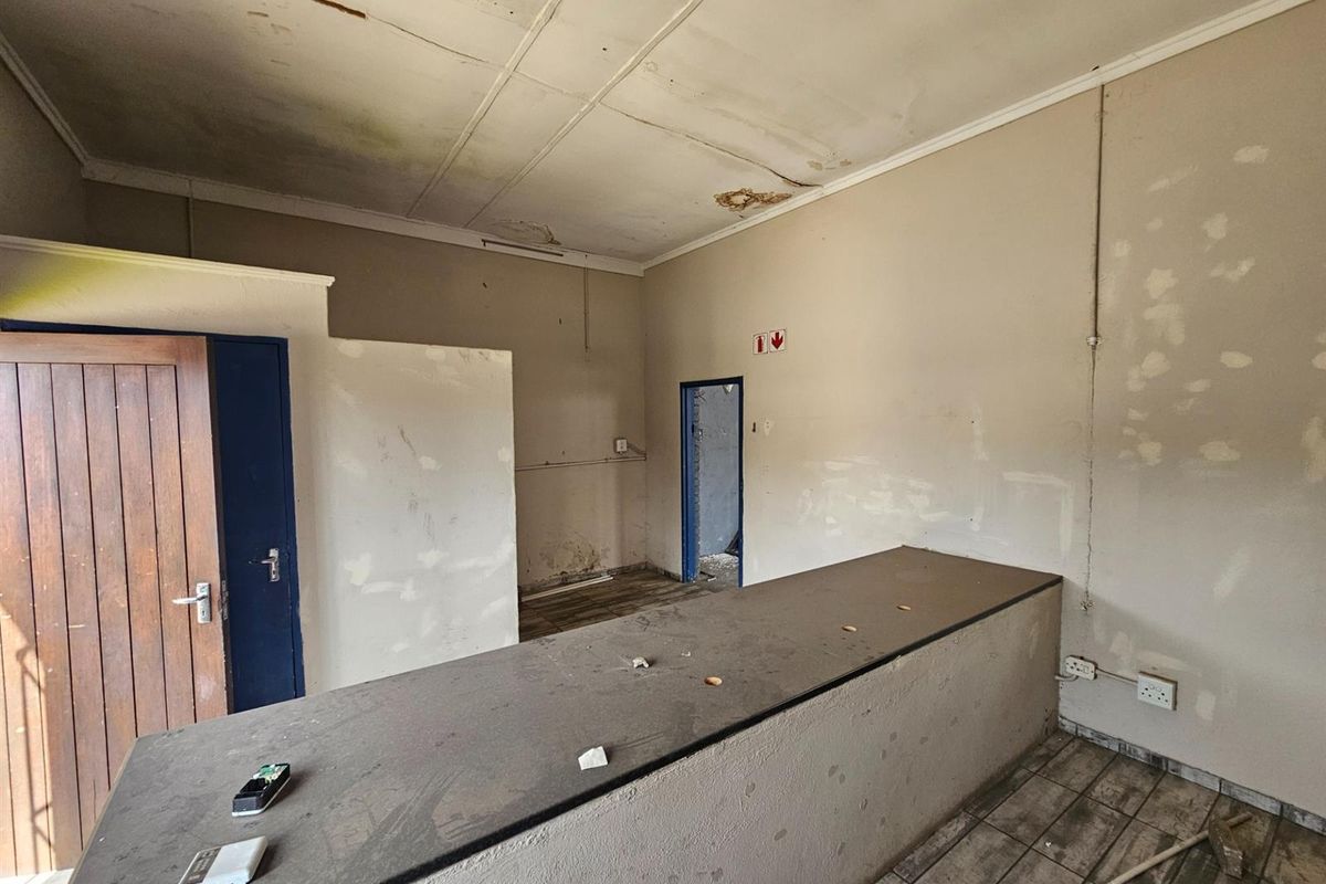 Industrial interior space featuring a built-in service counter, tiled flooring, and multiple access points, requiring significant renovation and cosmetic repairs.