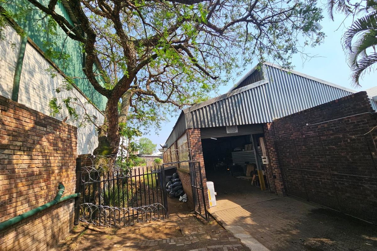 Exterior view of an industrial property featuring a brick facade, corrugated metal roof, and gated access to the warehouse entrance.
