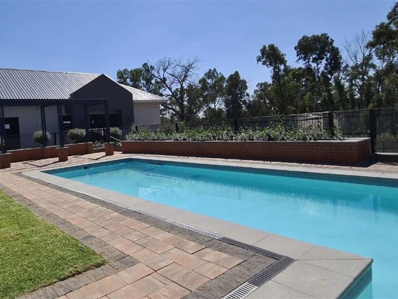 Outdoor pool area featuring a rectangular swimming pool, paved surround, brick planter box, and a metal pergola structure.