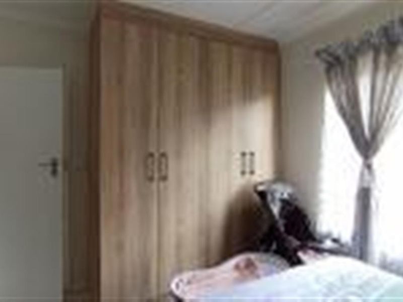 A bedroom featuring light wood-finish built-in cupboards and a window with curtains.