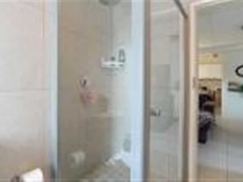 A functional bathroom featuring a glass-enclosed shower and tiled walls, with a view leading into the adjacent living area.