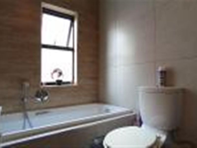 A functional bathroom featuring a bathtub, toilet, and neutral wall tiling with a window for natural light.